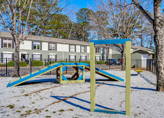 A playground with a blue and yellow slide in the foreground and apartment buildings in the background.