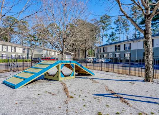 A playground with a blue and yellow slide in the foreground and apartment buildings in the background.