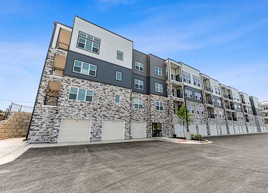 A modern apartment building with a stone facade and a parking lot in front.
