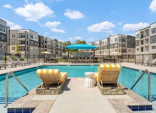 Two yellow and white striped sun loungers are on the edge of a pool.
