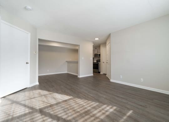 an empty living room and kitchen with white walls and wood flooring