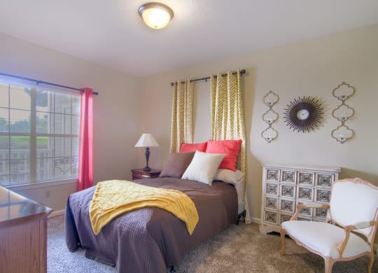 Enclave at Wolfchase Apartments in Cordova Tennessee photo of a bedroom with a bed and a chair in front of a window