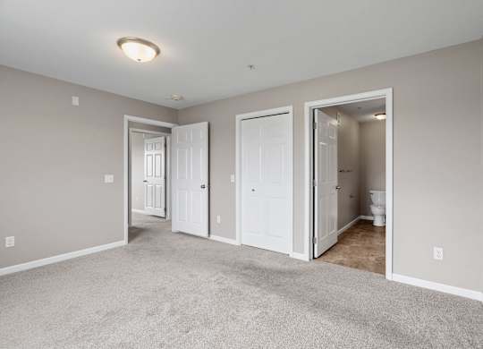 a bedroom with a carpeted floor and doors to a bathroom and a closet