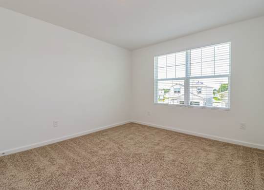 A room with a carpeted floor and a window showing a view of houses.