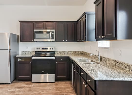 A kitchen with dark brown cabinets and a granite countertop.