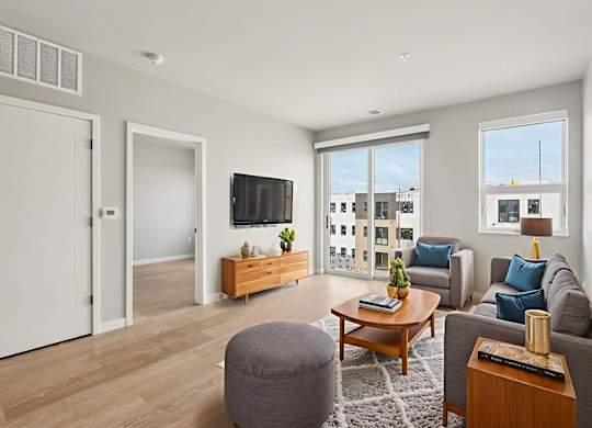 A living room with a grey sofa, a wooden coffee table, and a flat-screen TV mounted on the wall.