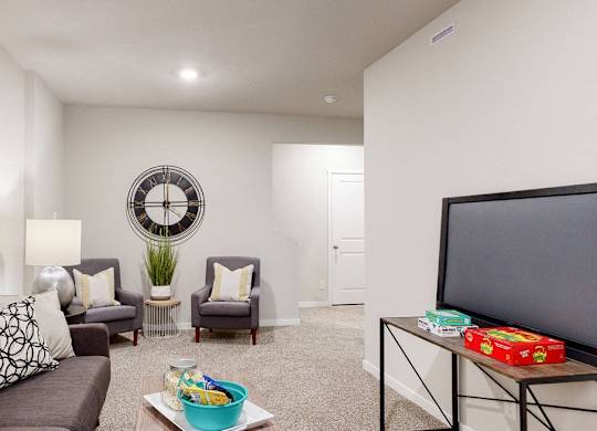 A living room with a grey couch, a yellow pillow, a white lamp, a round mirror, a small table with a box of tissues and a bowl of fruit.