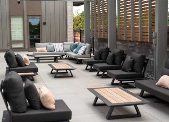 A patio with black cushioned furniture and wooden tables.
