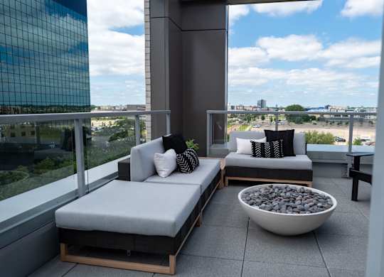 A balcony with two grey cushioned seats and a bowl of stones in the middle.