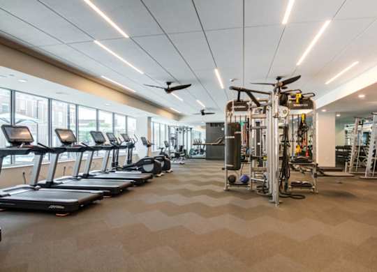 A spacious gym with treadmills, elliptical machines, and a weight training area.