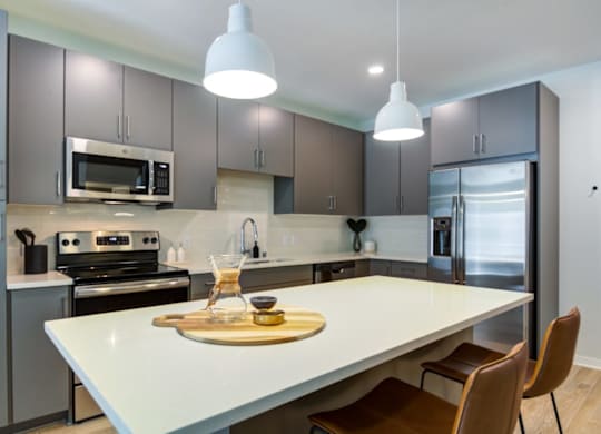 A modern kitchen with a white island and brown chairs.