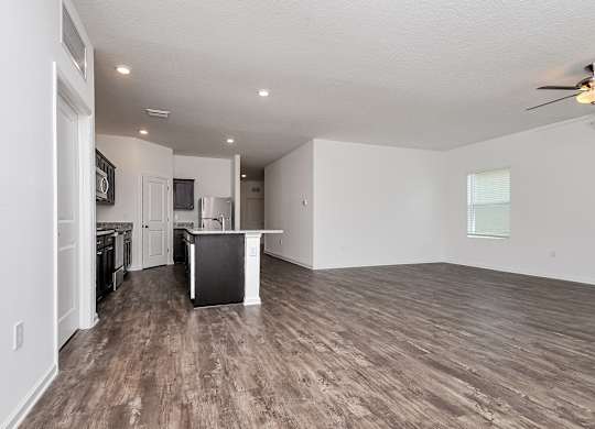 A spacious living room with a kitchen in the background.