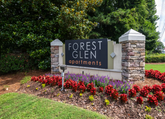a sign for forest glen apartments in front of a flower garden