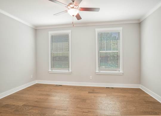 an empty room with a ceiling fan and two windows