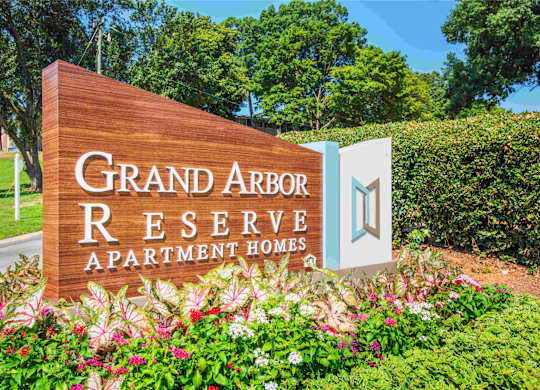 A sign for Grand Arbor Reserve Apartment Homes is displayed in front of a green hedge.