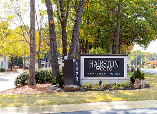 A sign for Hairston Woods Apartment Homes is in front of a row of trees.
