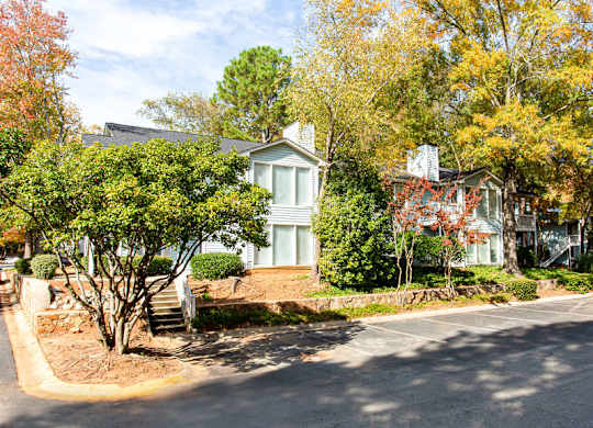 A house with a white door and windows is surrounded by trees with autumn leaves.