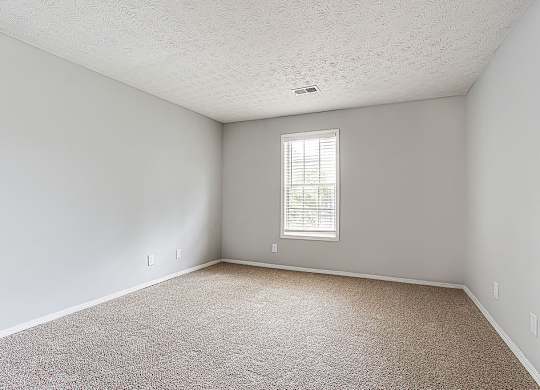A room with a carpeted floor and a window with blinds.
