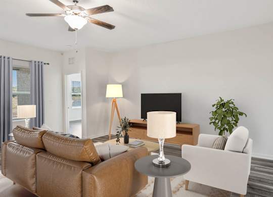 A living room with a brown sofa, a grey table, a black screen, a white chair, and a plant.