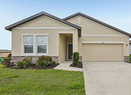 A beige house with a grey roof and a garage door.