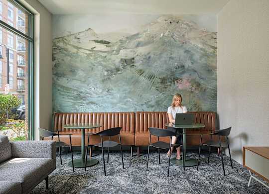 A woman is sitting at a table in front of a large painting.