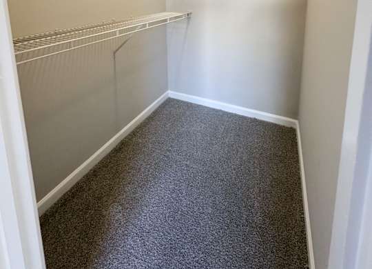 Empty walk in closet with white walls and grey carpet.