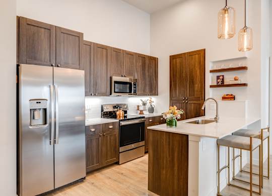 Greeley CO Pet-Friendly Luxury Apartments - The Shelby - Modern Ktichen with Wood-Style Cabinetry, White Quartz Countertops, Stainless Steel Appliances, Built-in Shelving, and Stool Seating