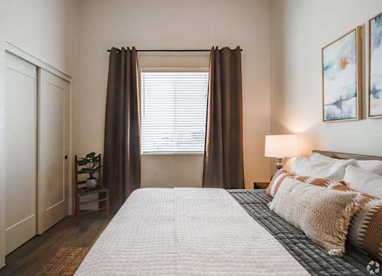 A bedroom with a large bed and a window with curtains.