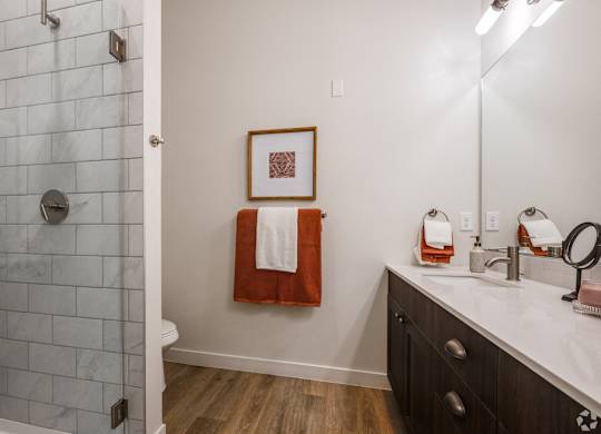 A bathroom with a white tiled shower and a white sink with a red towel hanging on the wall.
