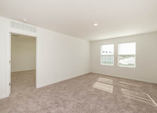 A large empty room with a carpet on the floor and a window showing a view of the outside.