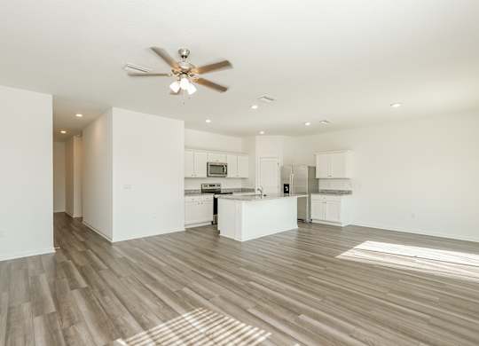 A spacious kitchen and living room with a ceiling fan and lighting.
