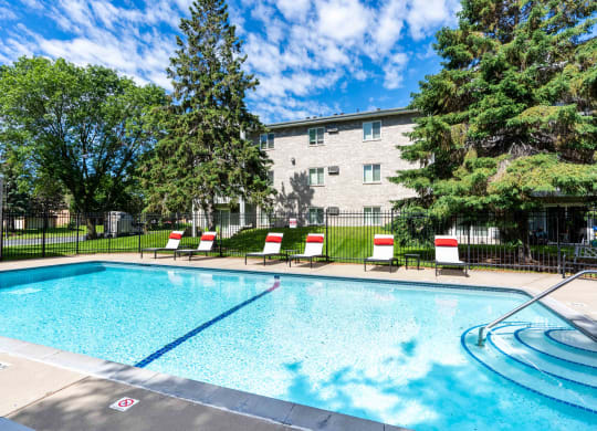 a swimming pool with chairs and a building in the background