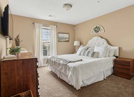 One, Two and Three- Bedroom Apartments for Rent in Sevierville, TN – Overlook at Allensville – A bedroom with a large bed, a dresser, and a window with curtains.
