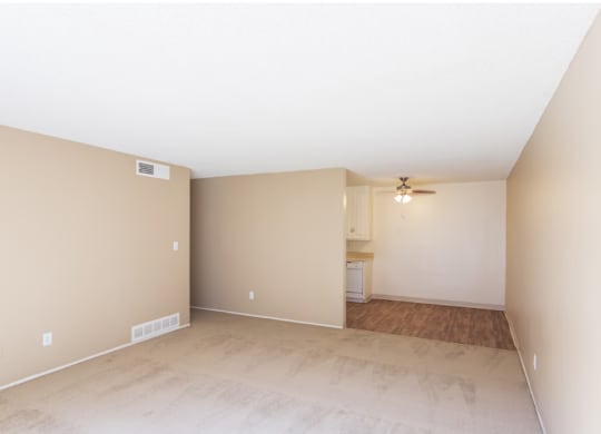 Two-Bedroom Apartments in El Cajon, CA - Ivanhoe Village - Unfurnished Living Room with Carpeted Flooring, Beige Walls, Ceiling Fan, and View of Kitchen.