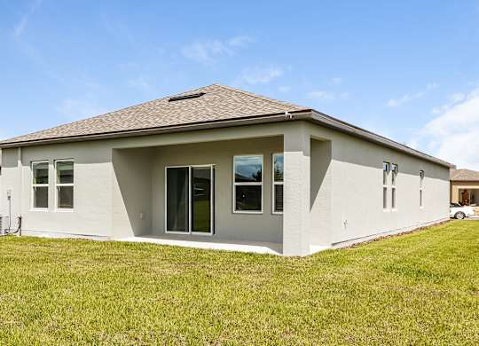 A house with a brown roof and white walls with a green lawn in front.