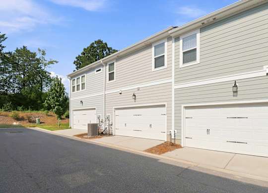 A two-story house with a grey siding and three white garage doors.