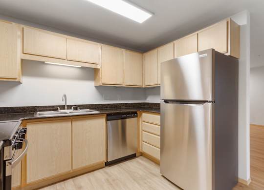 A kitchen with a stainless steel refrigerator and wooden cabinets.