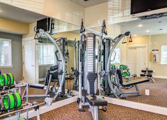 Apartments For Rent in Vancouver, WA - Reflections at the Park - 24-Hour Fitness Center With Workout Equipment, Mirror Walls, And TV Screen.