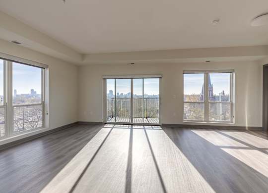 A spacious room with wooden floors and large windows overlooking a cityscape.