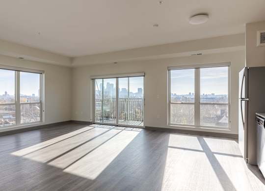A large, empty room with wooden floors and a view of the city through large windows.