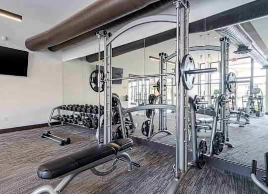 A gym with a variety of equipment including a bench press, dumbbells, and a squat rack.