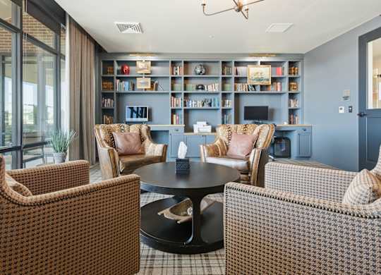 A living room with a black coffee table surrounded by brown patterned chairs and a bookshelf filled with books.