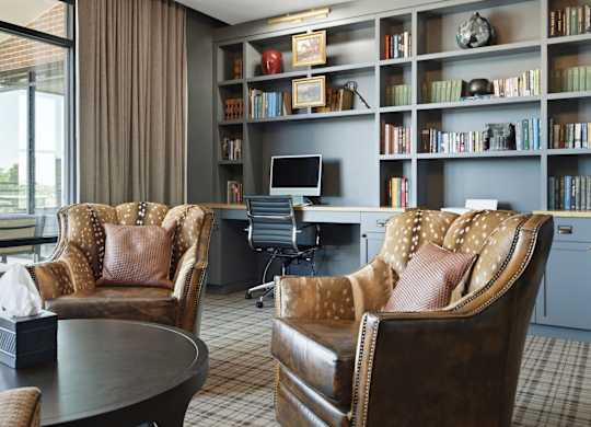 Two leather chairs with a desk and bookshelf in the background.