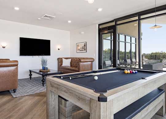 A pool table is in the middle of a room with leather chairs and a television.