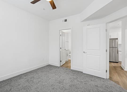 A room with a ceiling fan and a door leading to a kitchen.