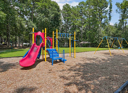 A playground with a red slide, blue and yellow swings, and a yellow and blue climbing frame.