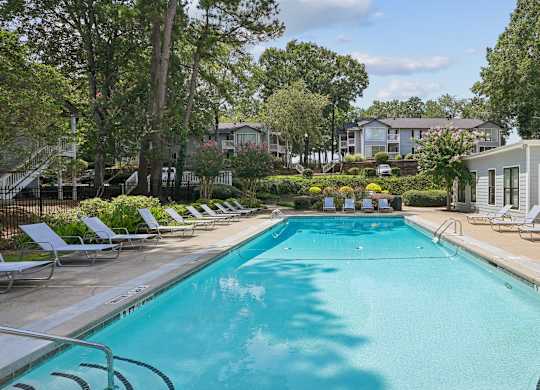 A swimming pool surrounded by lounge chairs and trees.