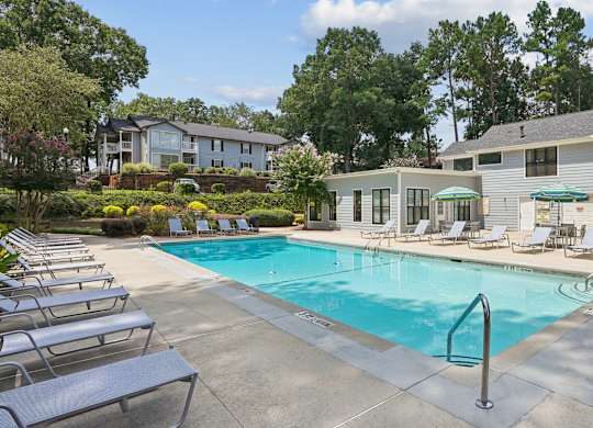 A swimming pool surrounded by lounge chairs and trees.