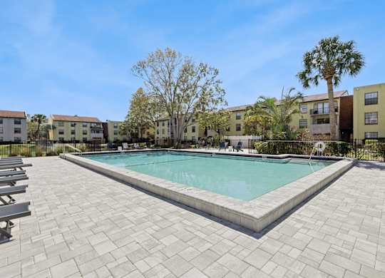 A swimming pool surrounded by a brick patio and palm trees.