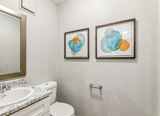 A bathroom with a toilet, sink, and two framed artworks on the wall.